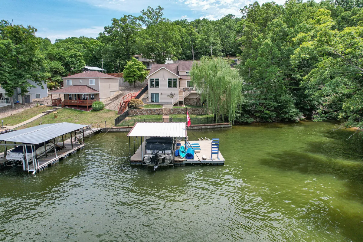 A lakefront dock scene with the house in the background, large windows, and lush green trees. The setting evokes tranquility and the potential for curated adventures, from morning coffee by the water to sunset relaxation.