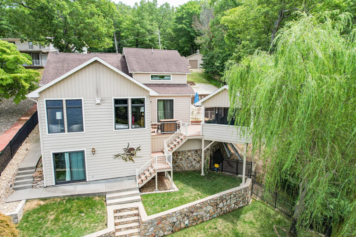 An exterior shot of the property featuring large windows, a welcoming staircase, a stone wall, and lush surrounding greenery. The image suggests inviting entryways and the connection between indoor comfort and outdoor beauty.