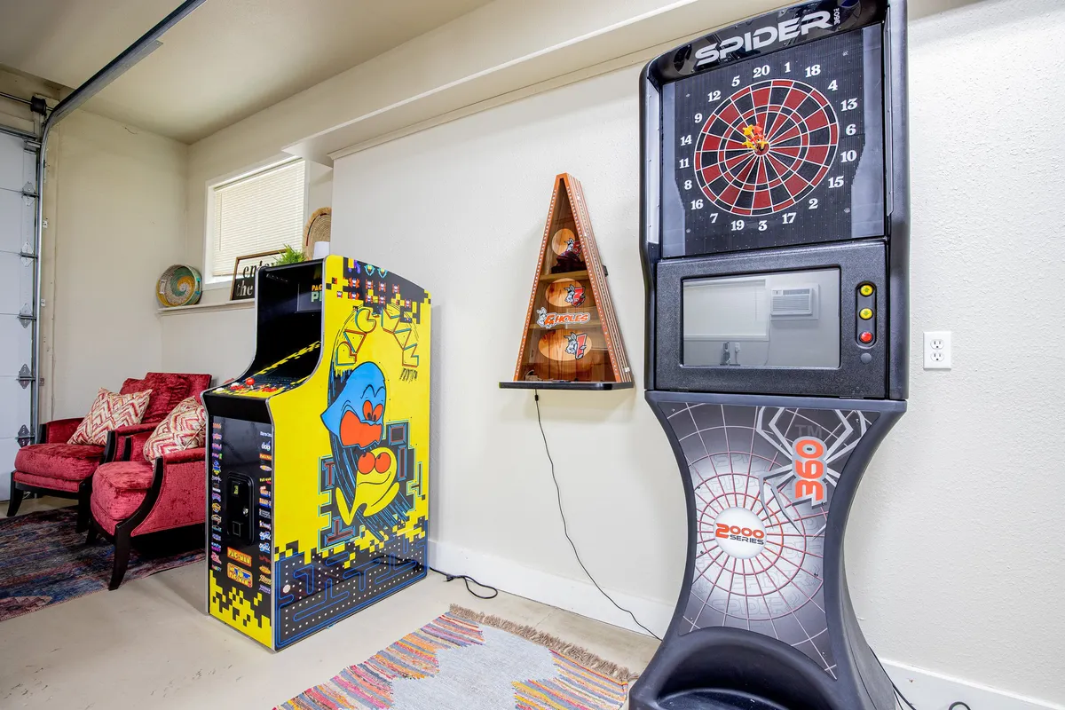 A lively game room interior with a dartboard machine, arcade game, red chairs, and a colorful rug. The space looks energetic and fun, perfectly embodying the atmosphere described for family game nights or competitive adult gatherings.