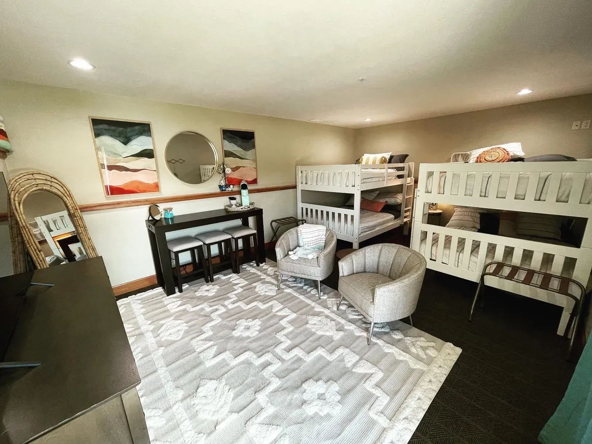A playful bunk room with multiple bunk beds, a seating area, colorful rugs, and wall art. The space exudes a fun, family-friendly vibe—perfect for sleepovers, late-night chats, or relaxing after a day of play.