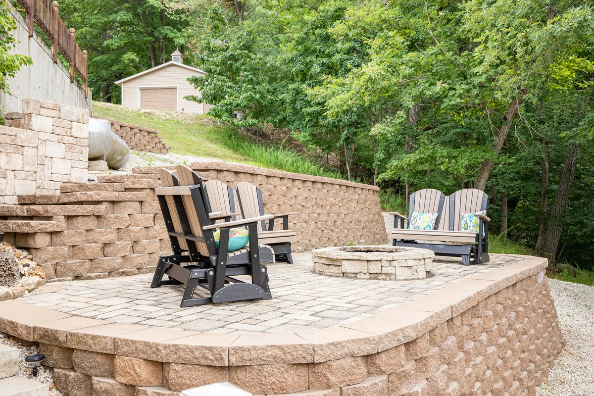 A cozy outdoor fire pit area surrounded by Adirondack chairs and a rustic stone wall. The setup is perfect for socializing, relaxing, or enjoying stargazing evenings by the fire, fostering a sense of warmth and togetherness.