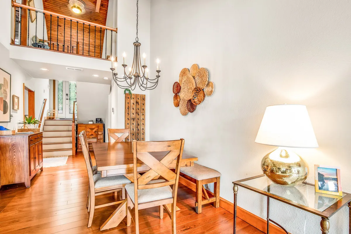 A dining area with a large table and chandelier offers a cozy setting for meals. Woven wall art and a softly-lit lamp enhance the inviting ambiance, making it ideal for family breakfasts or evening dinners.