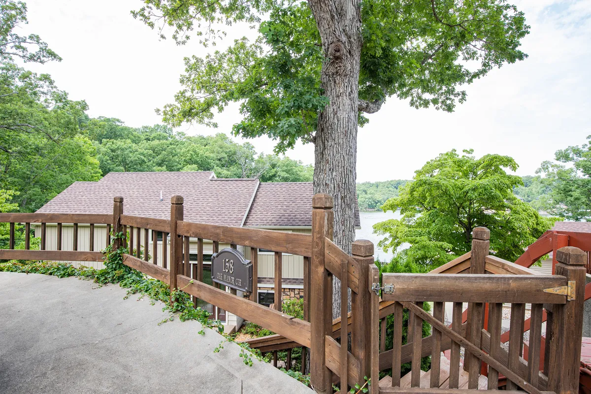 This image shows an elevated wooden railing overlooking a large tree, a sign reading '158', and a beautiful view of the lake beyond. Natural surroundings including mature trees and the lakeshore create a serene, welcoming environment ideal for outdoor activities.